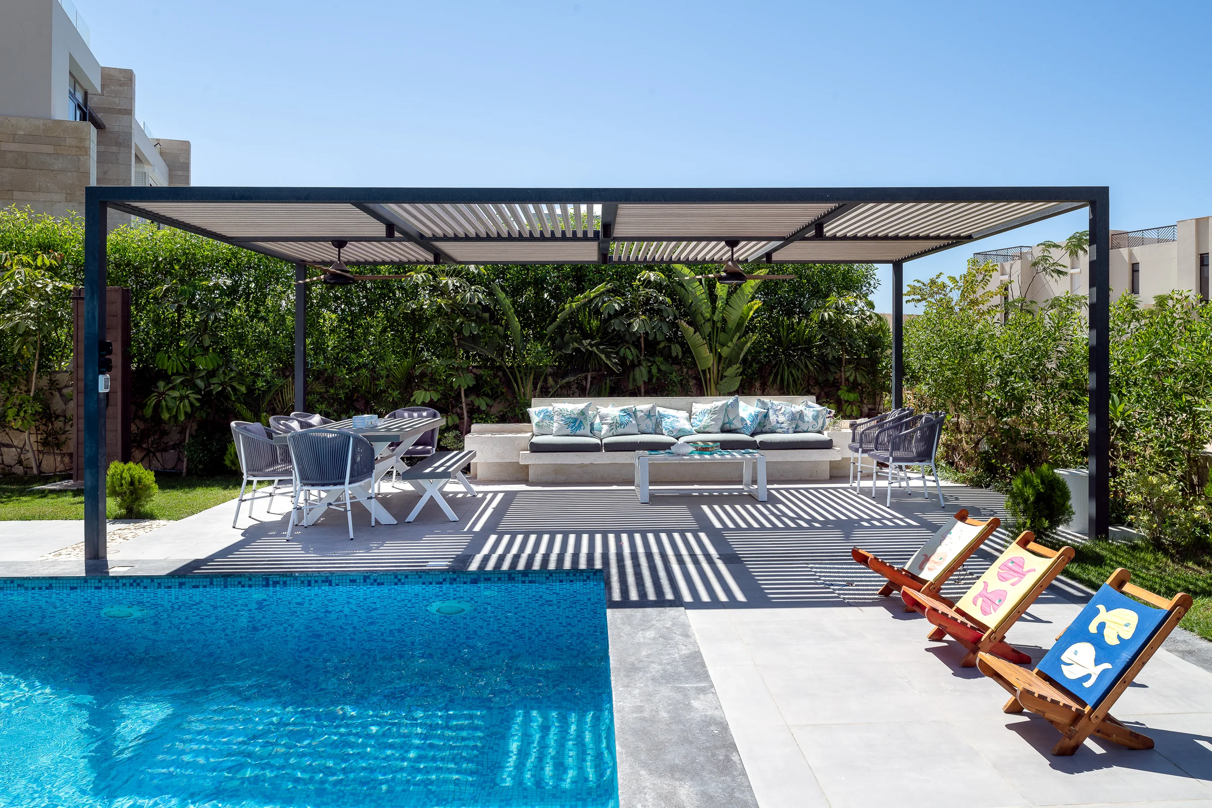 The pergola from the lawn, loungers along the pool edge.
