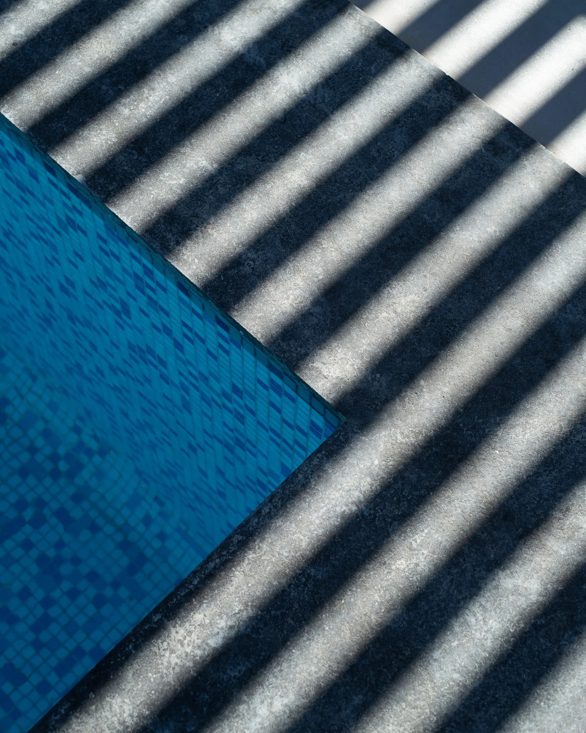 Close detail: pool mosaic meeting stone in raking light.