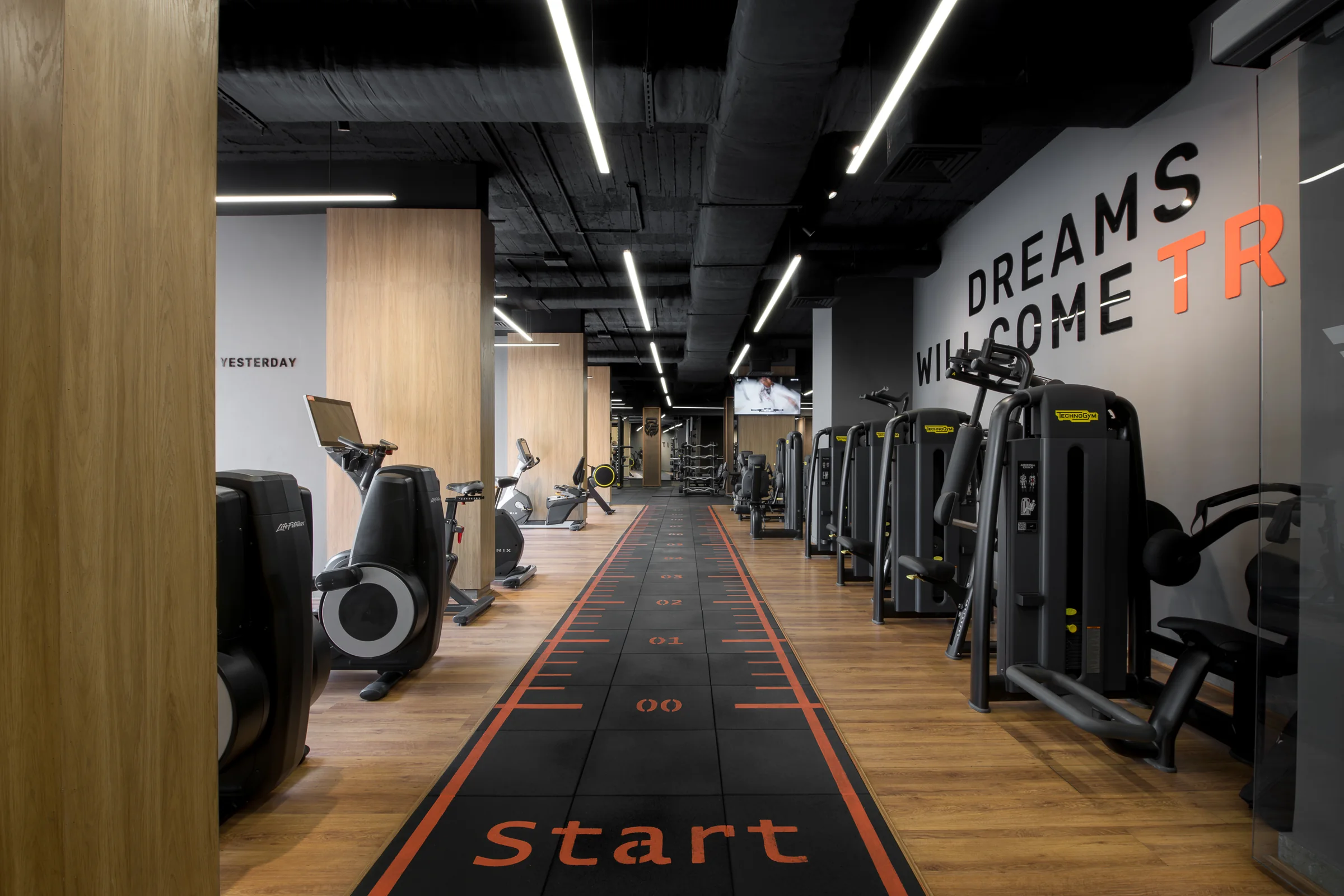The cardio floor along the printed running track, oak wall on the left.