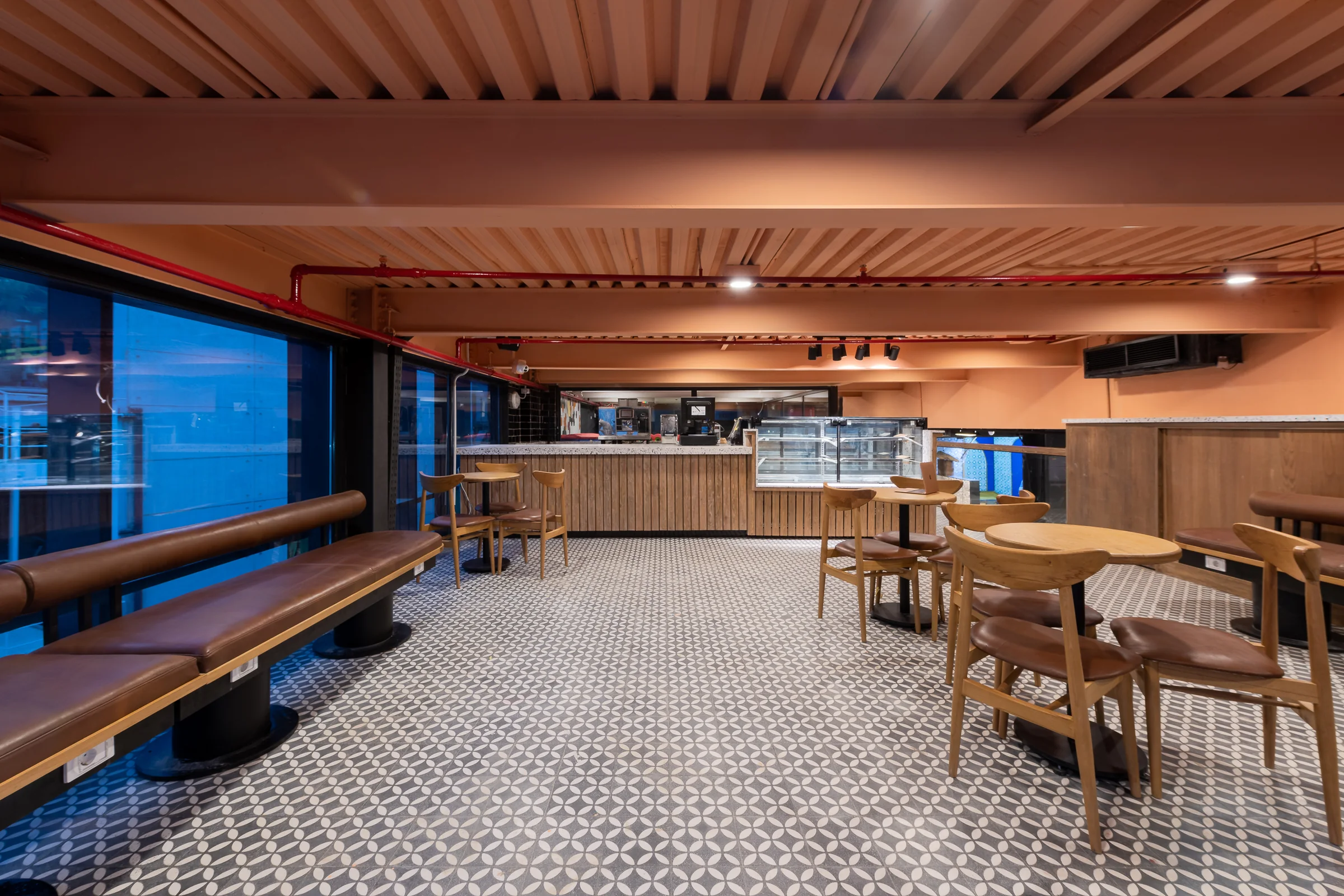 Seating area with banquettes and timber tables, glazing behind.