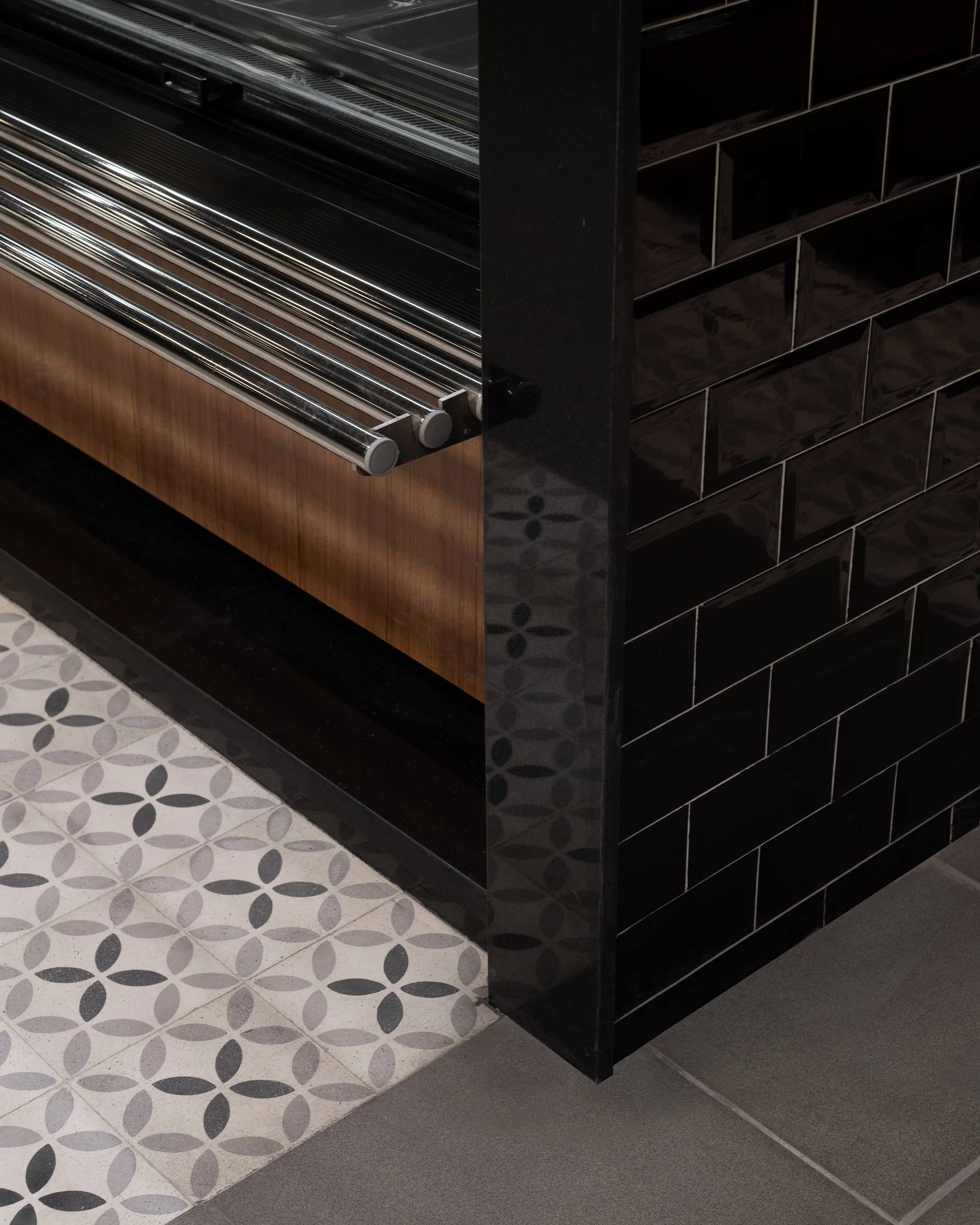 Detail: timber, black tile and patterned floor meeting at a corner.