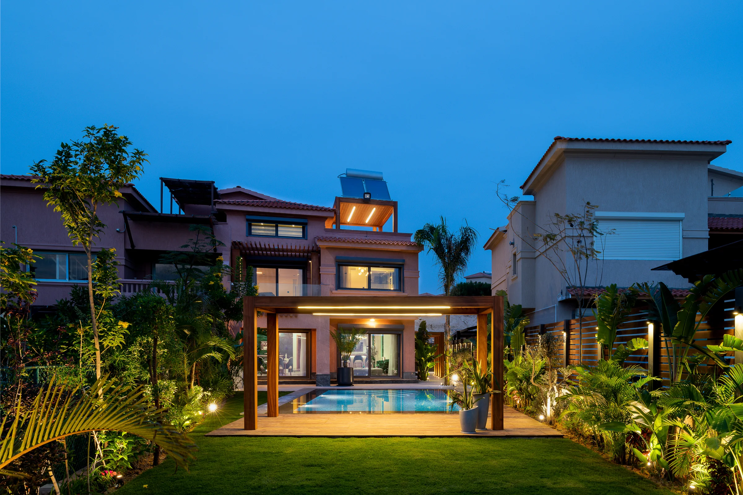 The villa at blue hour, pergola and lit pool in the foreground.