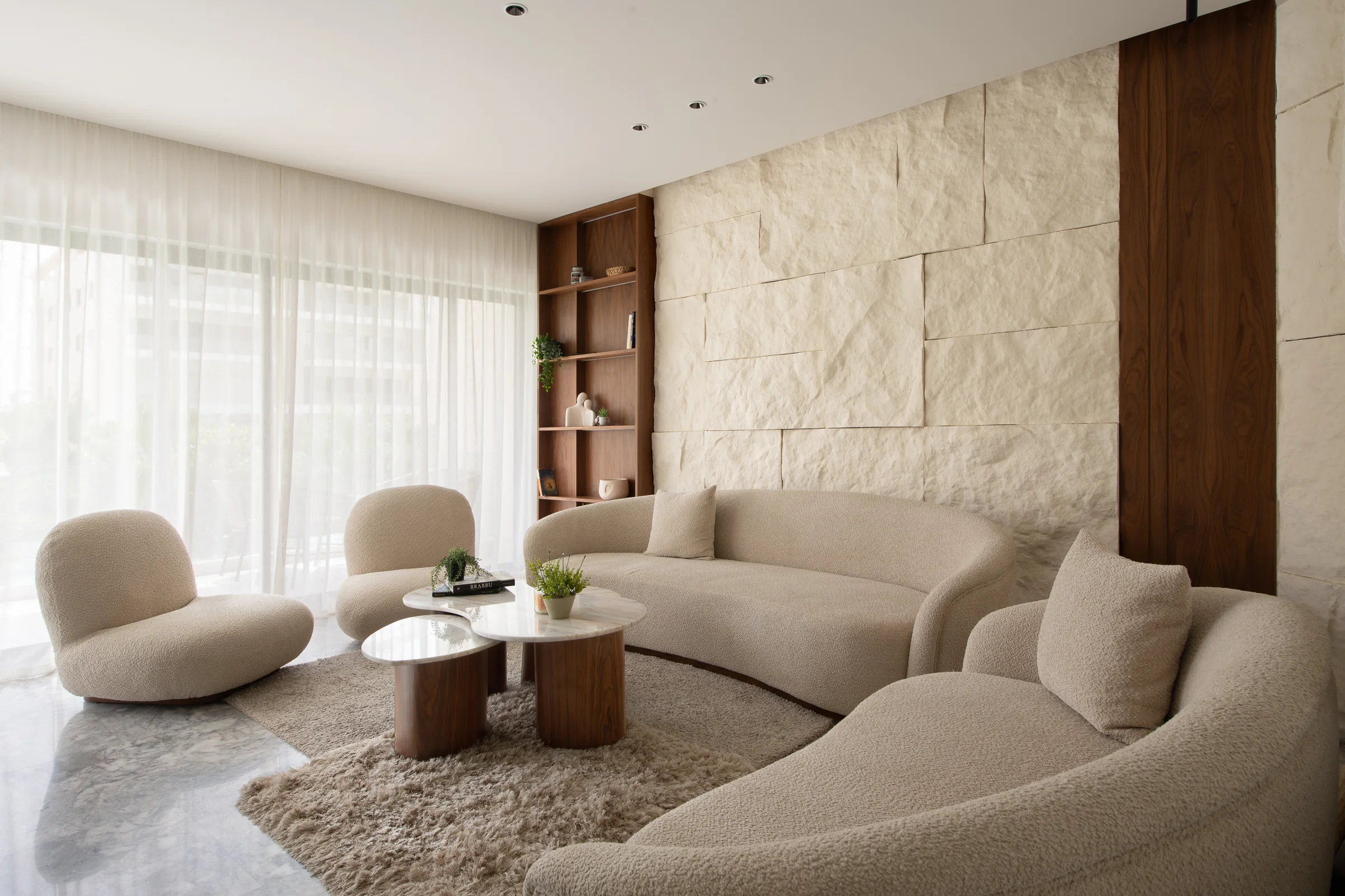 Curved bouclé seating in the living room against a carved stone wall.