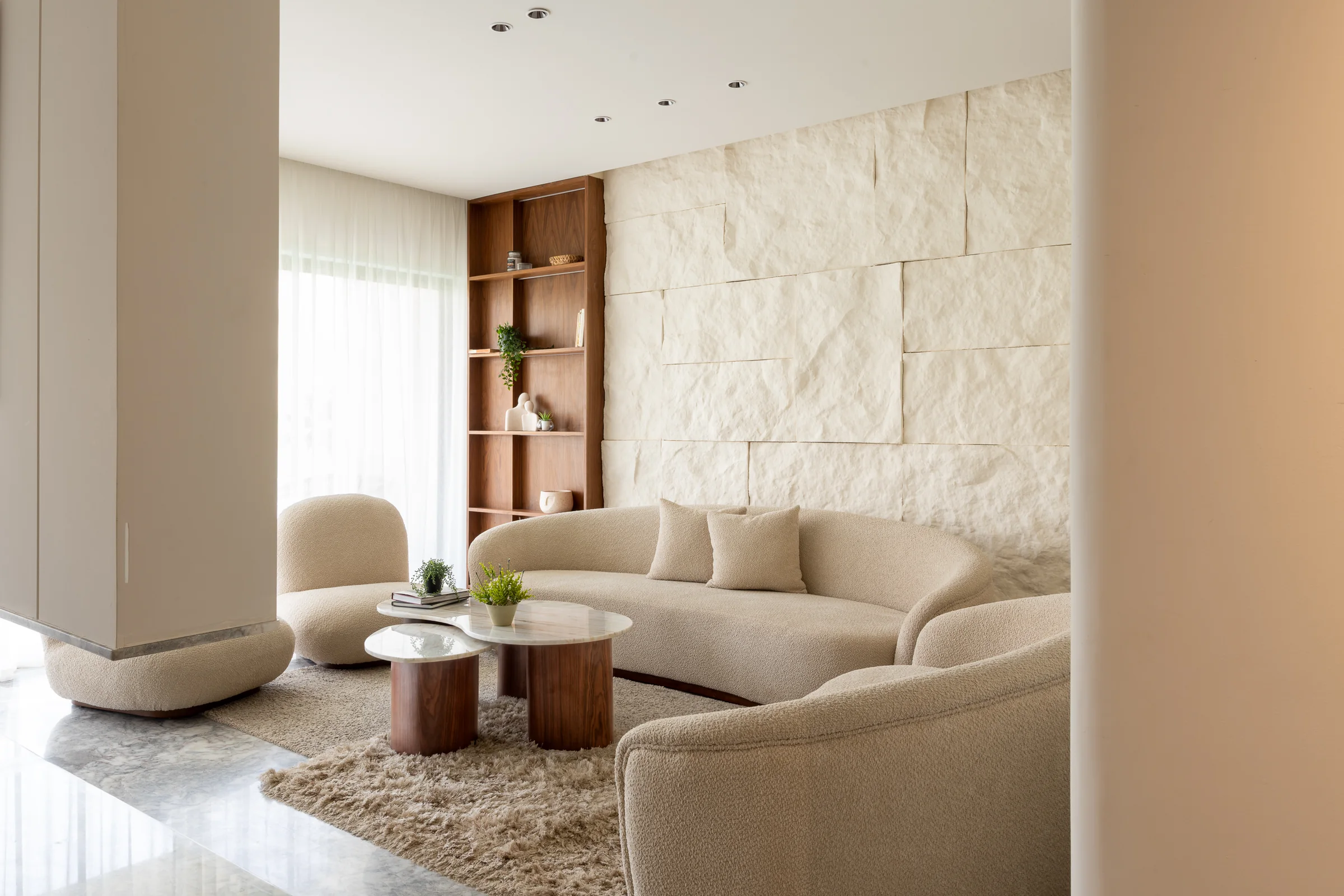 Long living room: low sofa, stone wall, light through full-height sheers.