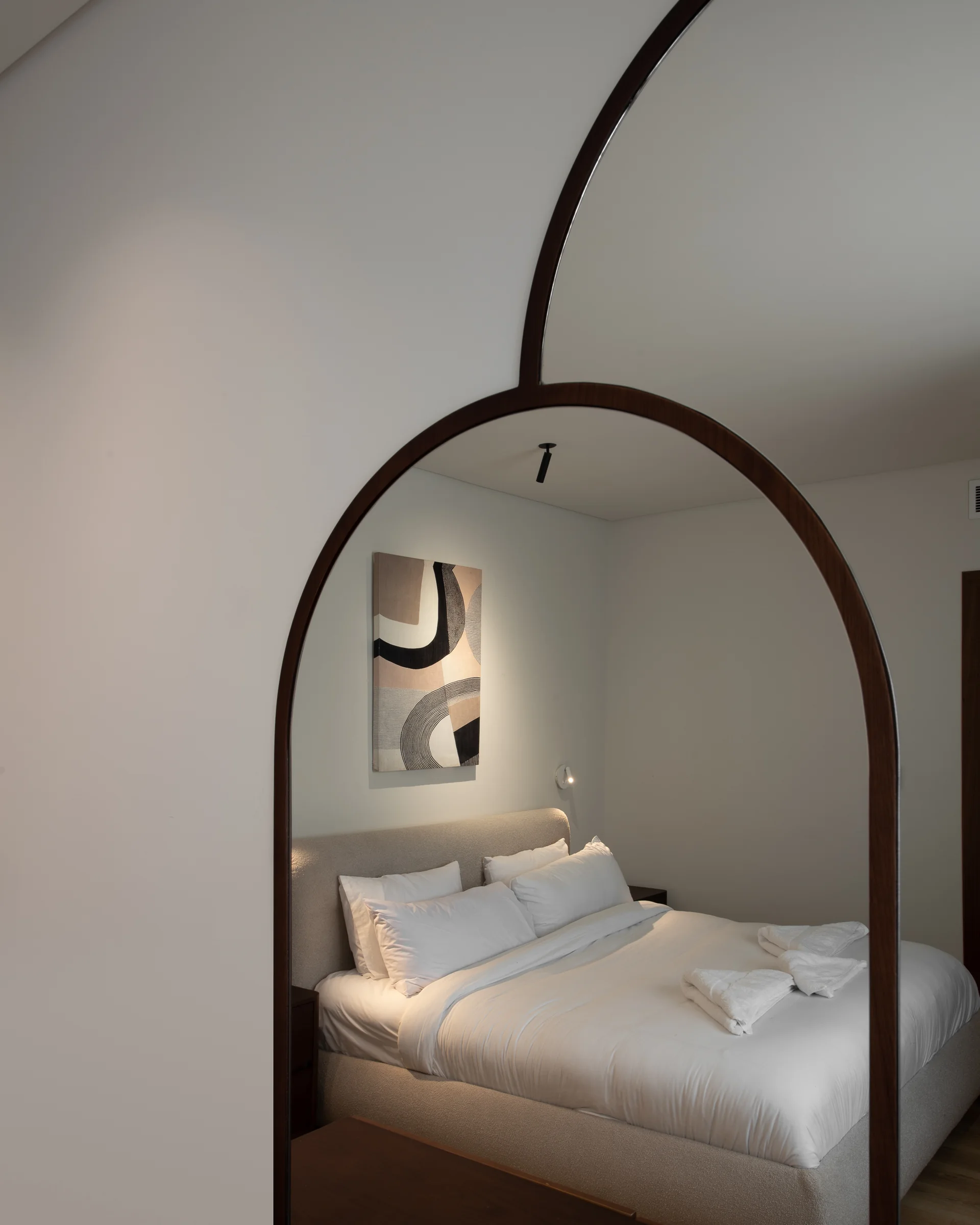 Arched mirror beside the bed, plaster and shadow.