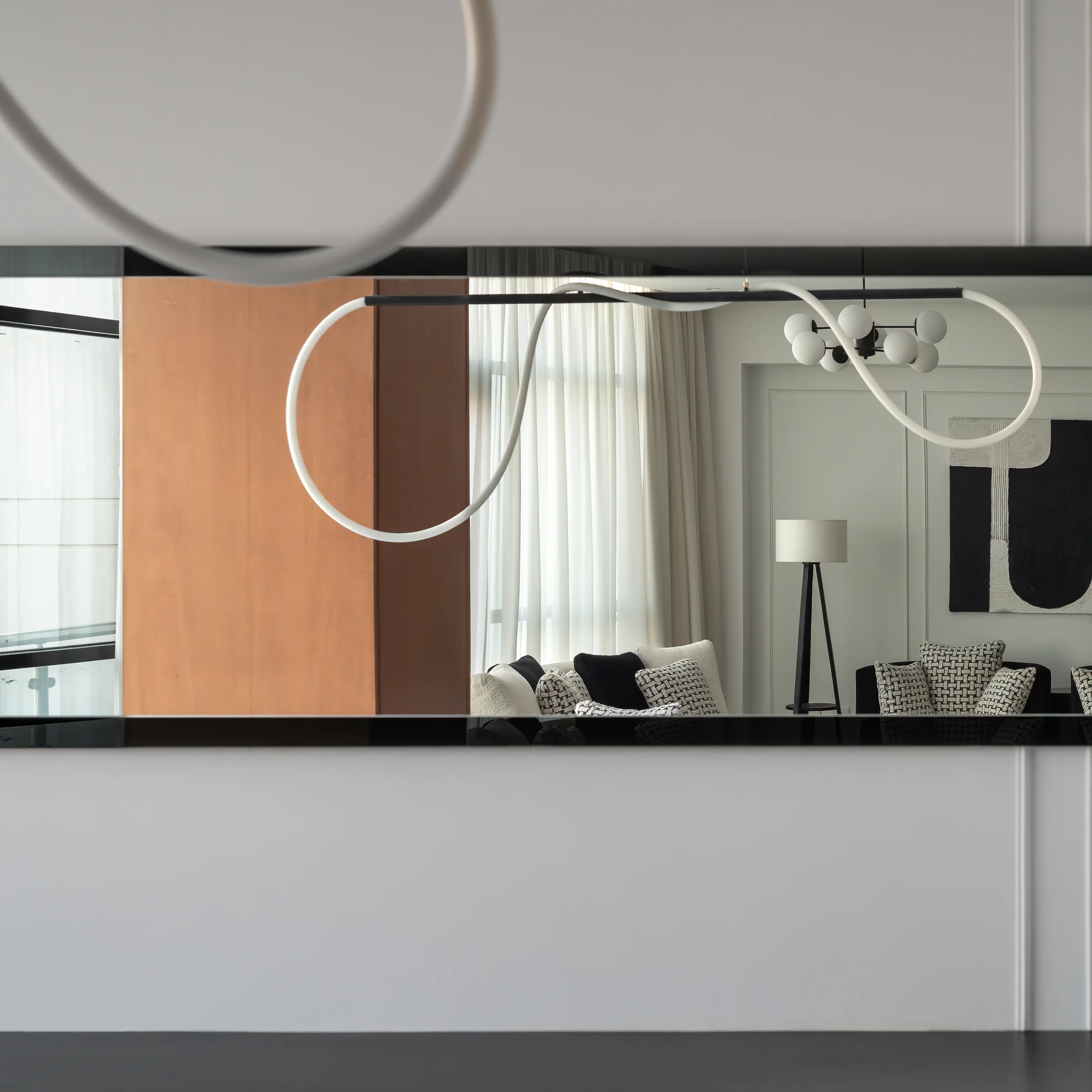 The room reflected in a long mirror with a looping light fitting.