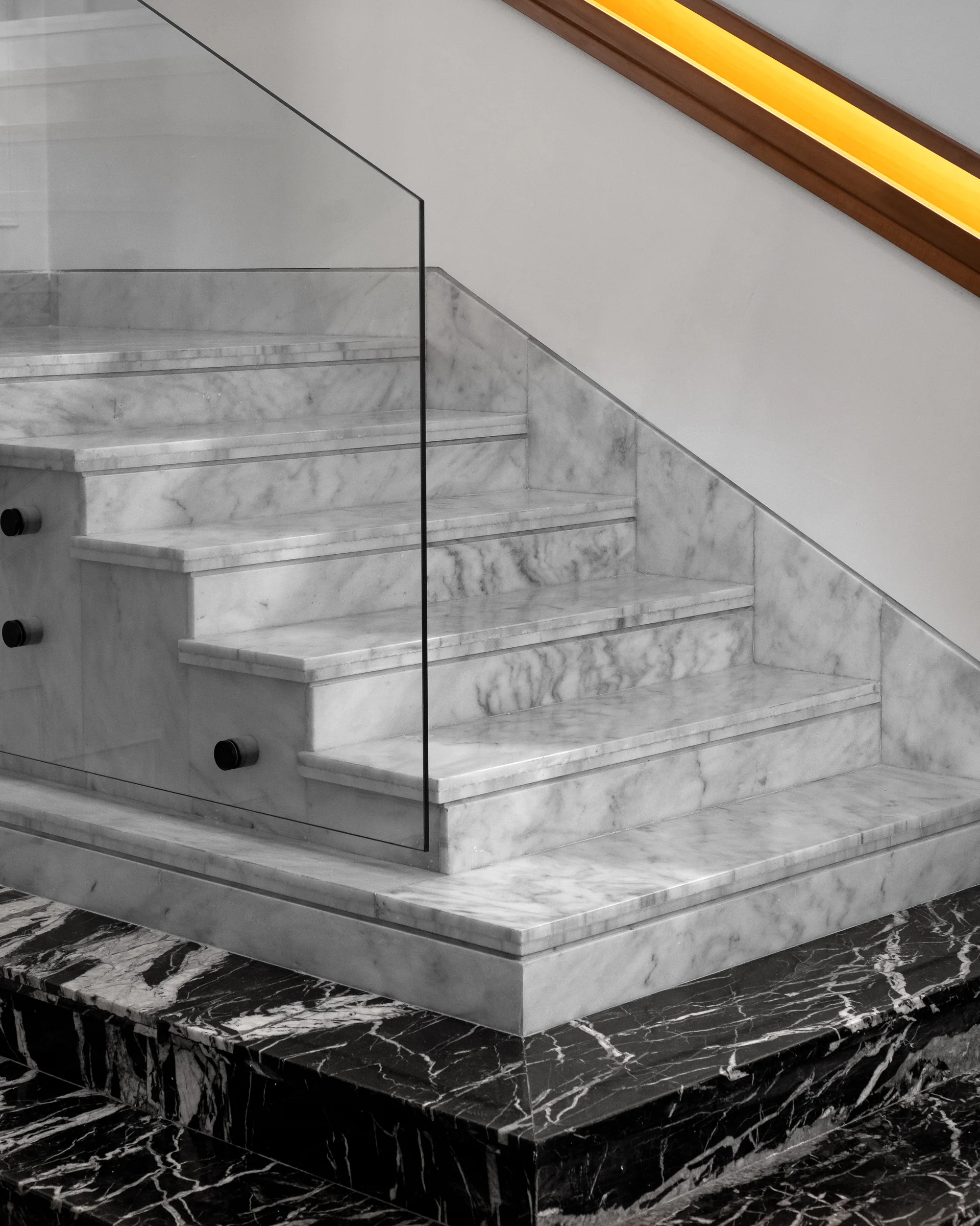Stair flight with a glass balustrade over black marble.