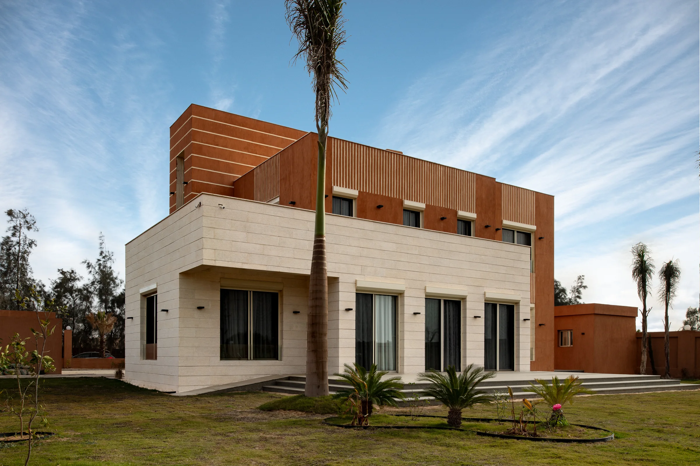 Three-quarter view from the lawn with a mature palm crossing the facade.