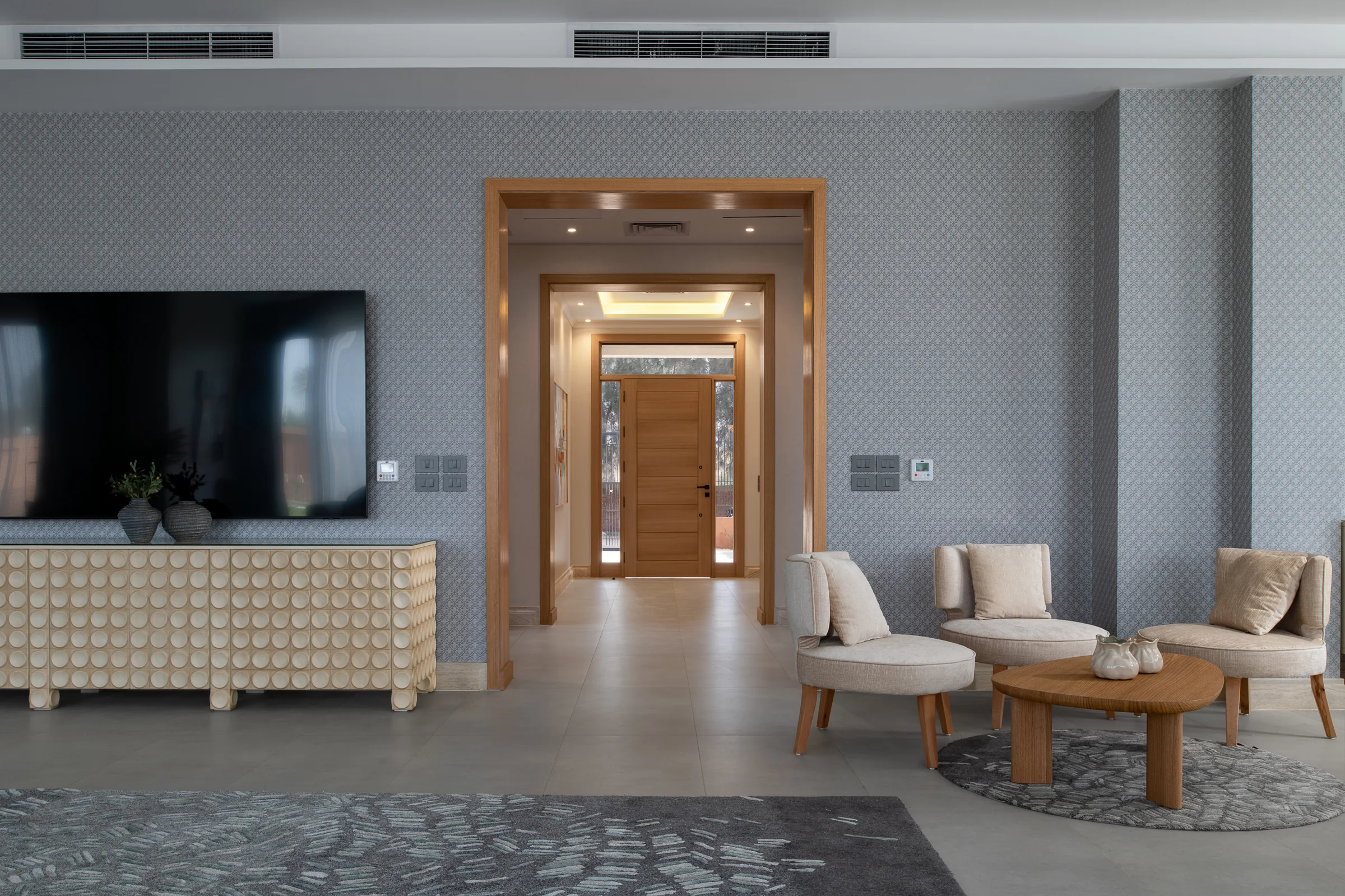 Living room television wall in patterned wallpaper, with the entrance hall beyond.