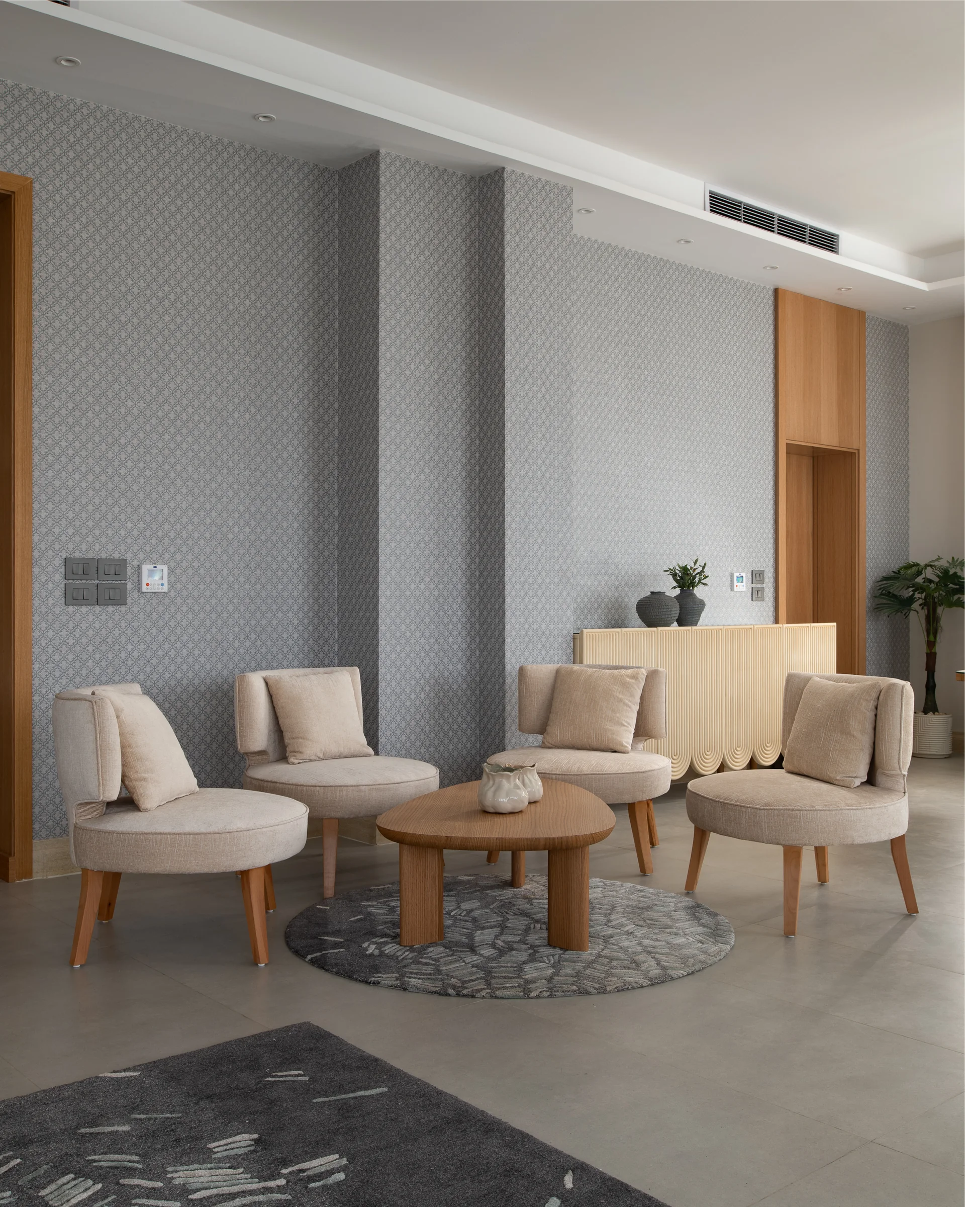 Four upholstered lounge chairs around a low oak table on a round rug.