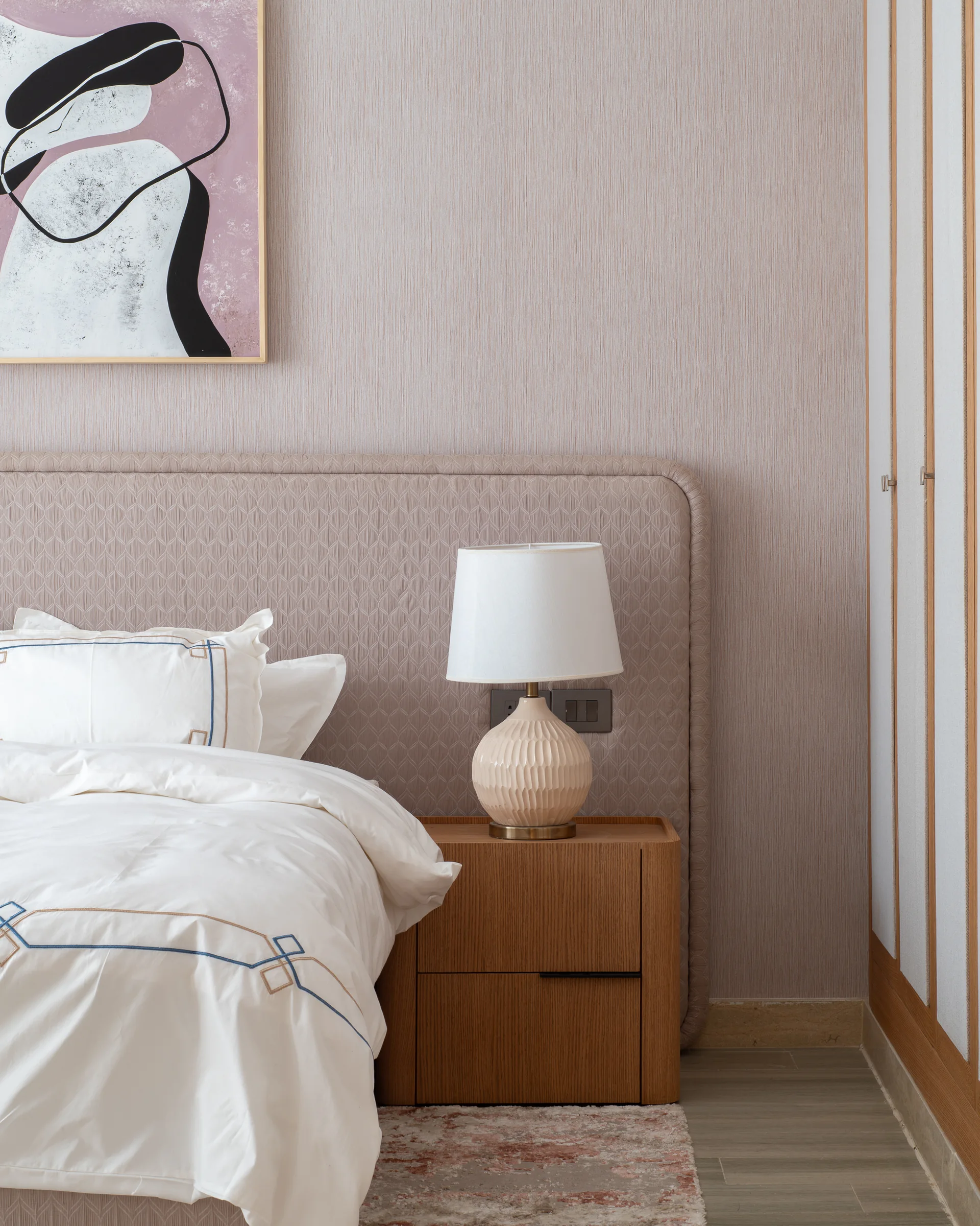 Corner of a bedroom with a patterned headboard and oak bedside table.