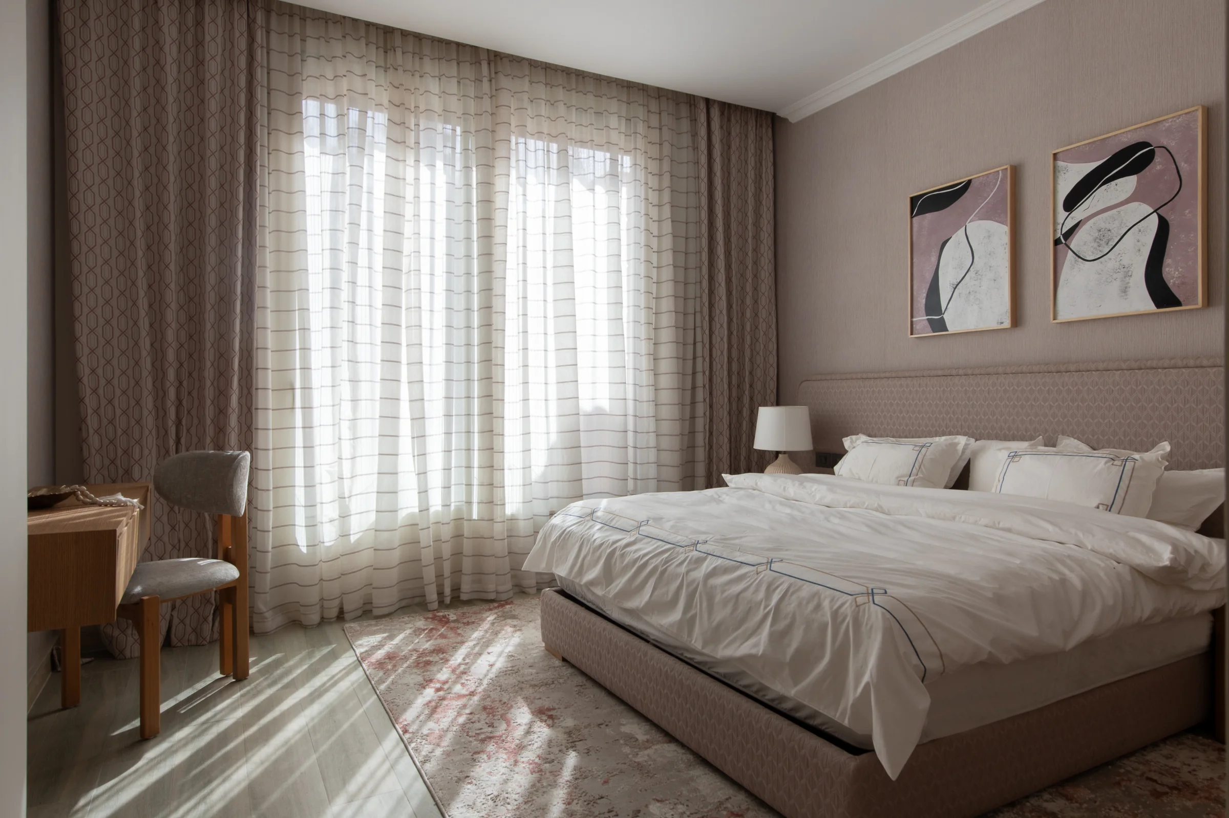 Bedroom with a desk under framed art and curtains along two walls.