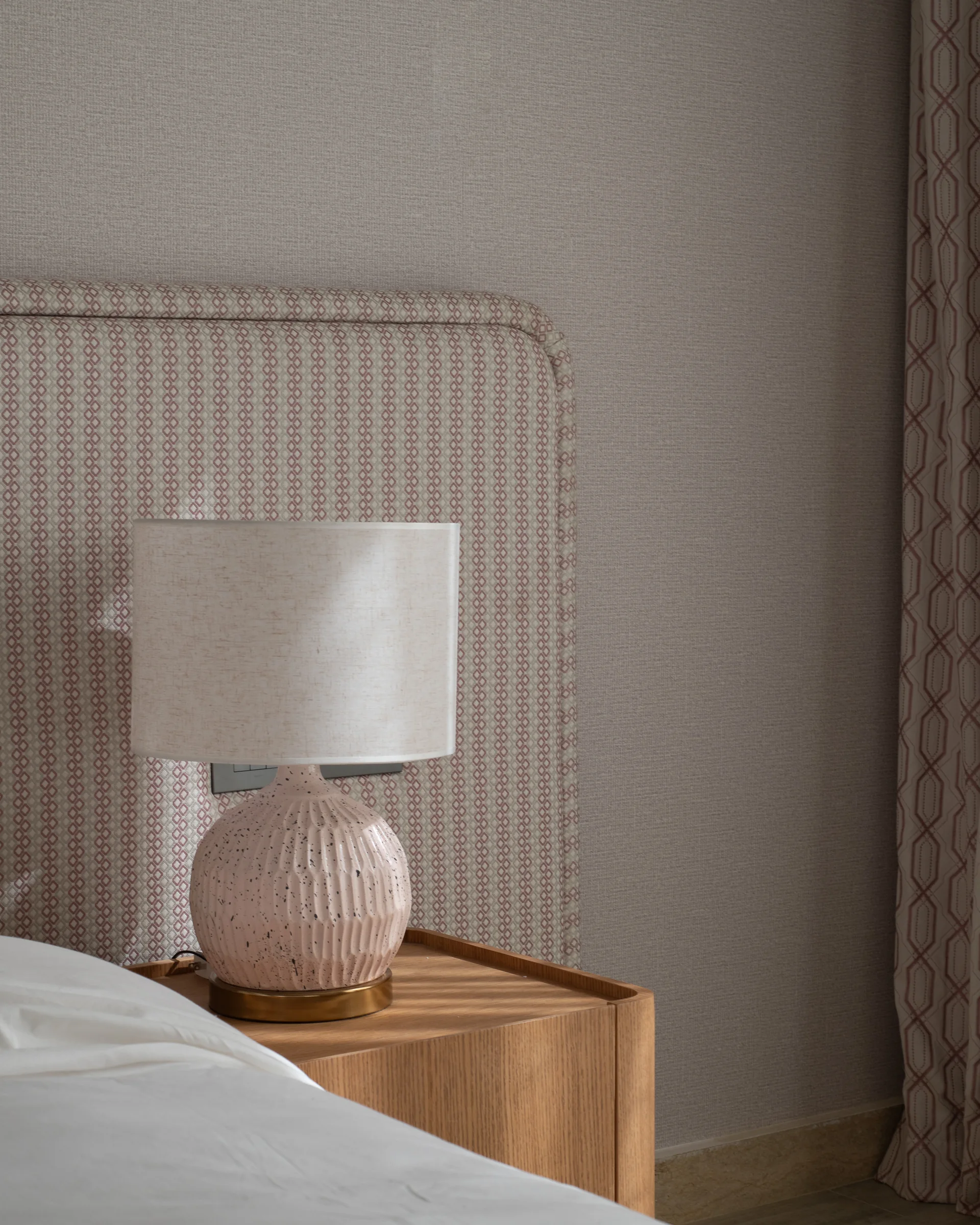 Ceramic bedside lamp against a patterned upholstered headboard.