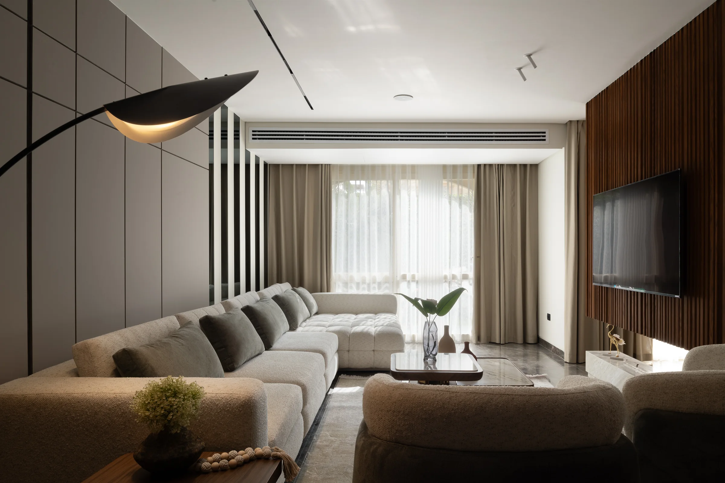 Living room with a black arc floor lamp, sculptural sofa and walnut panelling.