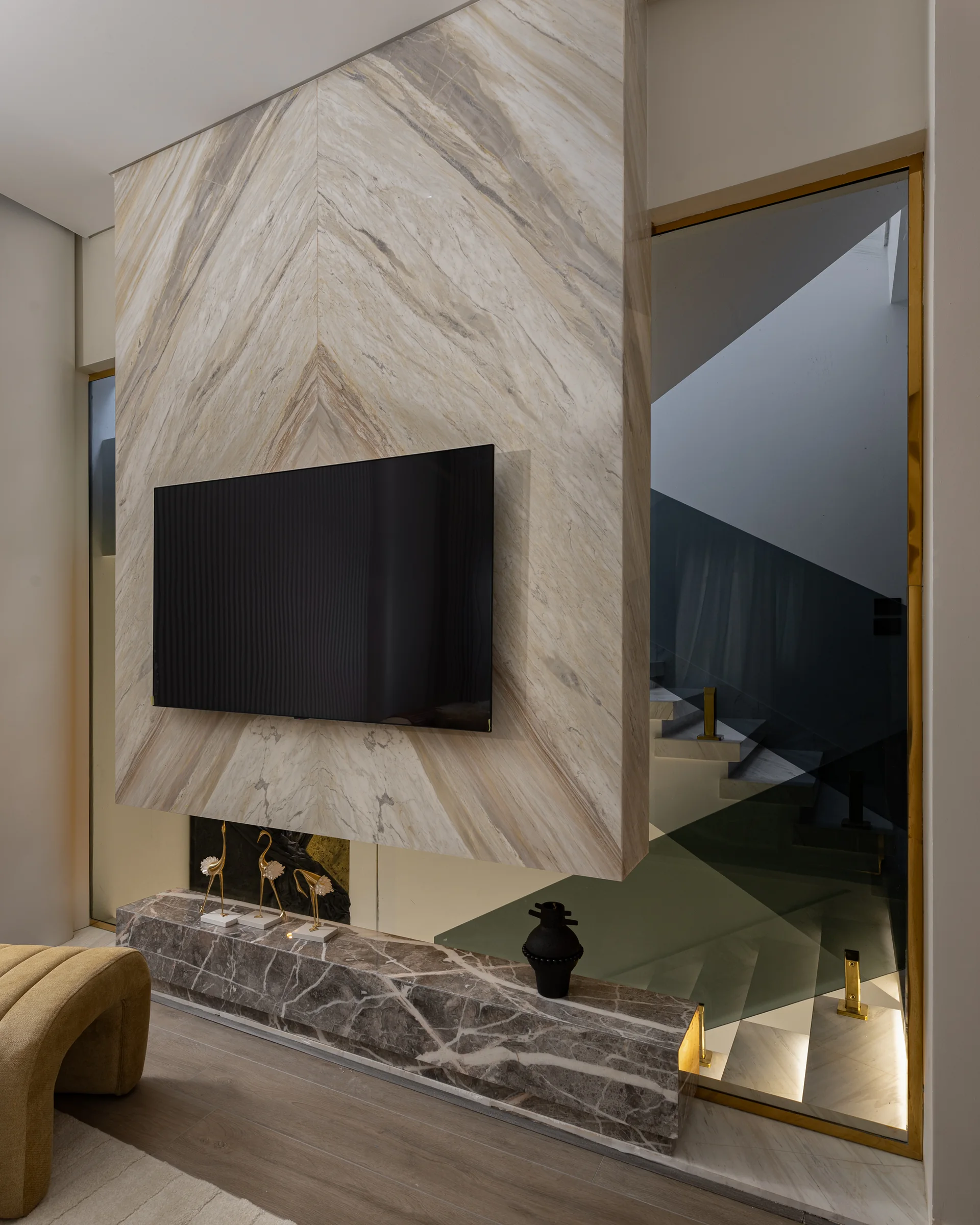 Book-matched marble media wall with a brass-framed mirror return.