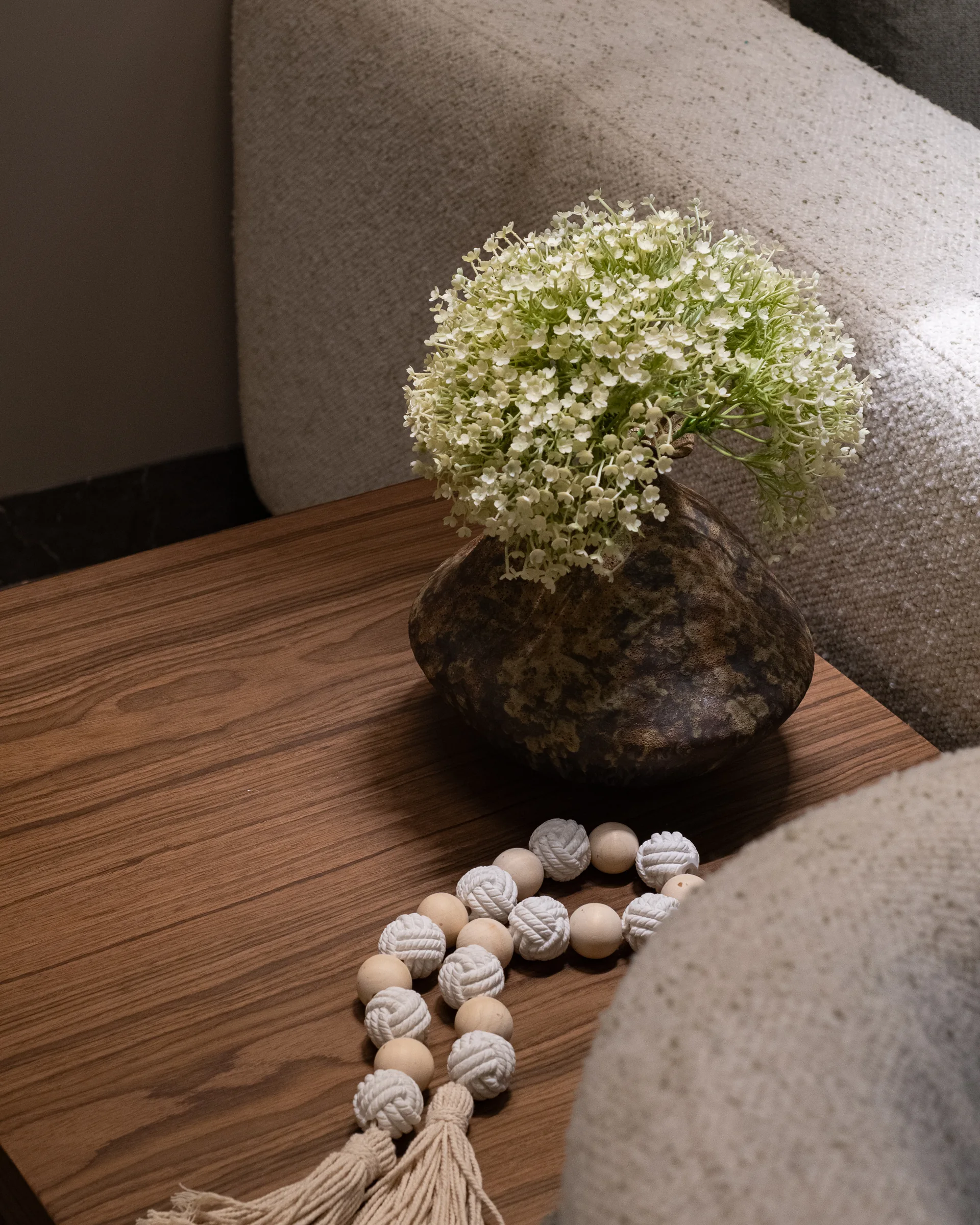 Close detail: ceramic vase and beads on a walnut surface.