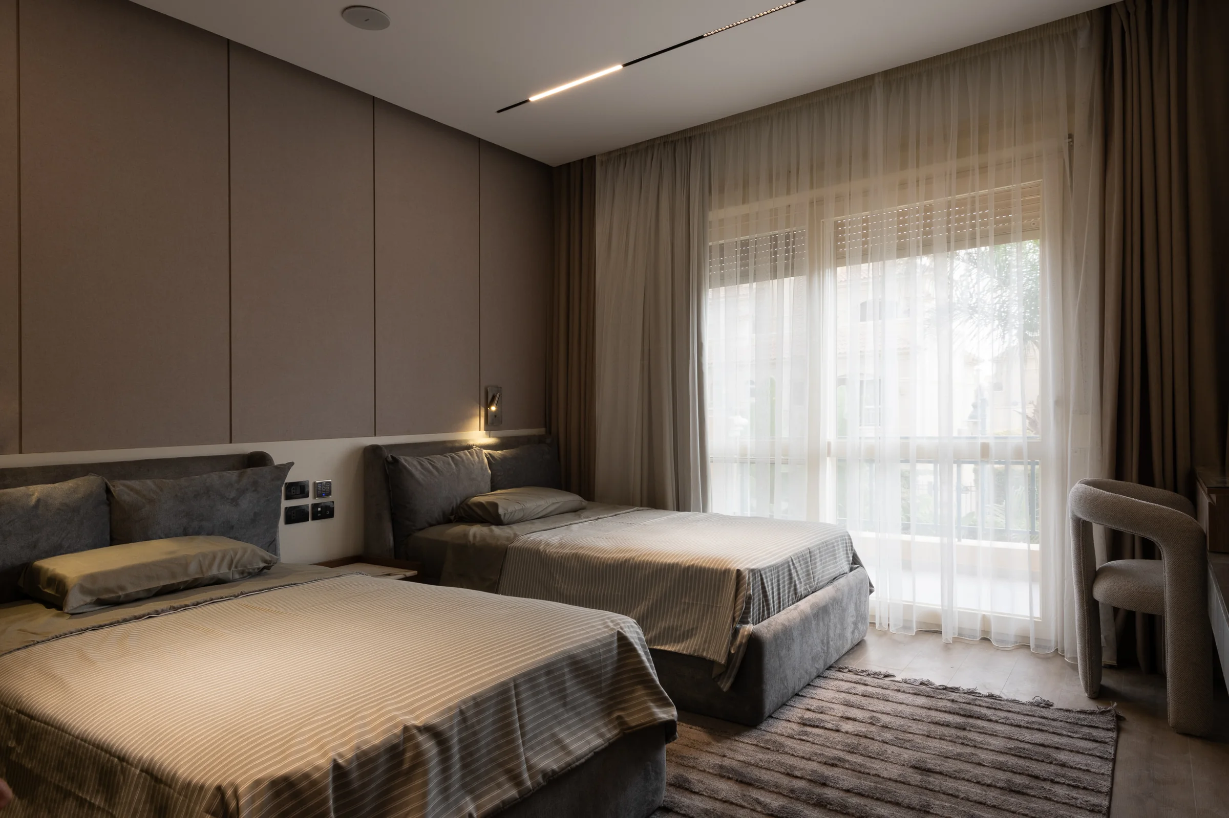 Bedroom with an upholstered headboard wall and morning light at the window.