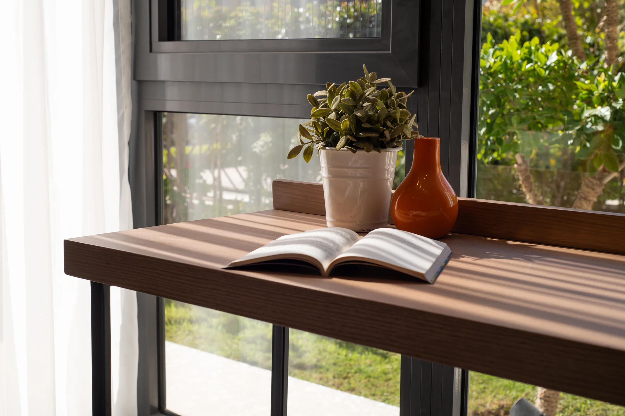 The desk from the side, garden through the glass.