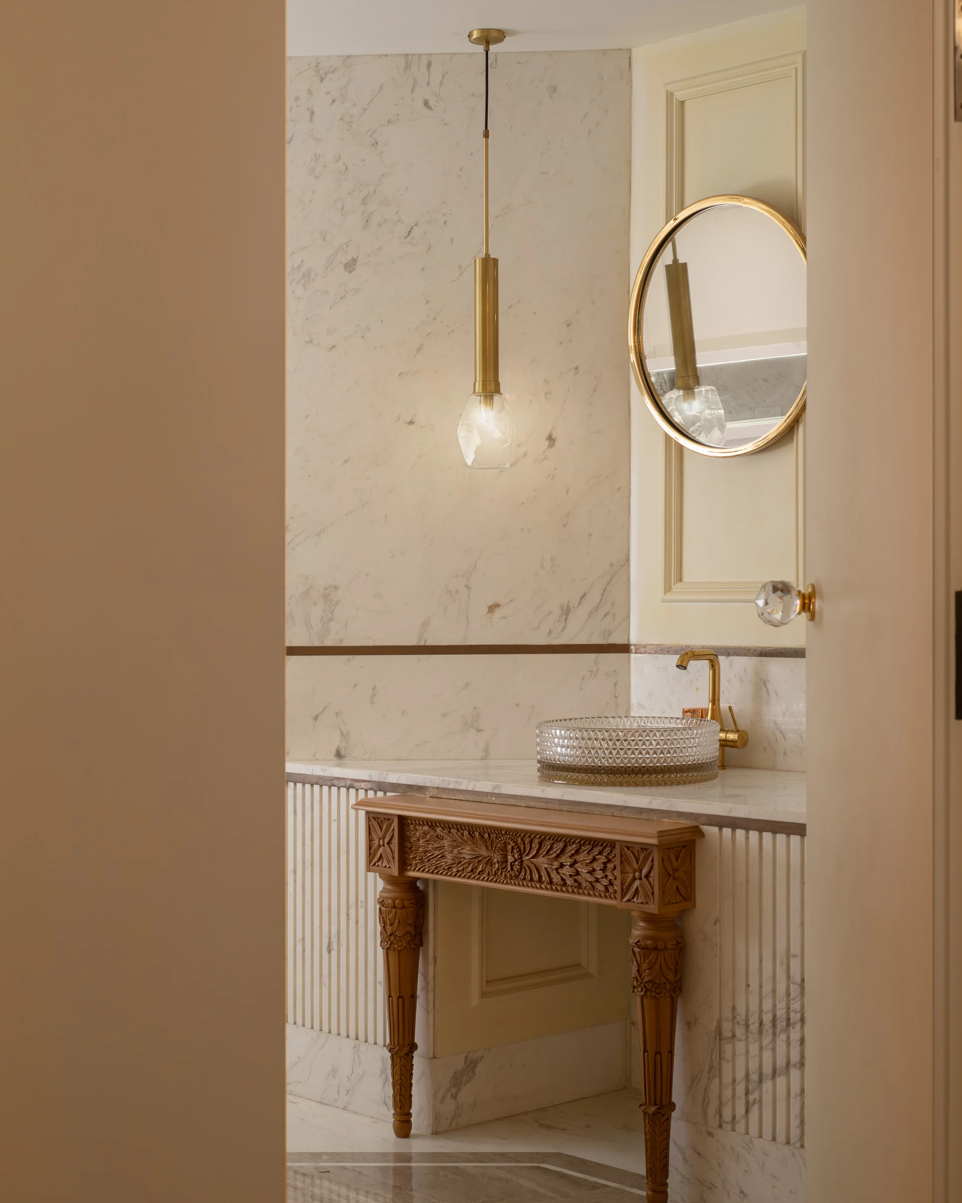 Entrance console in marble under a brass pendant, round mirror above.