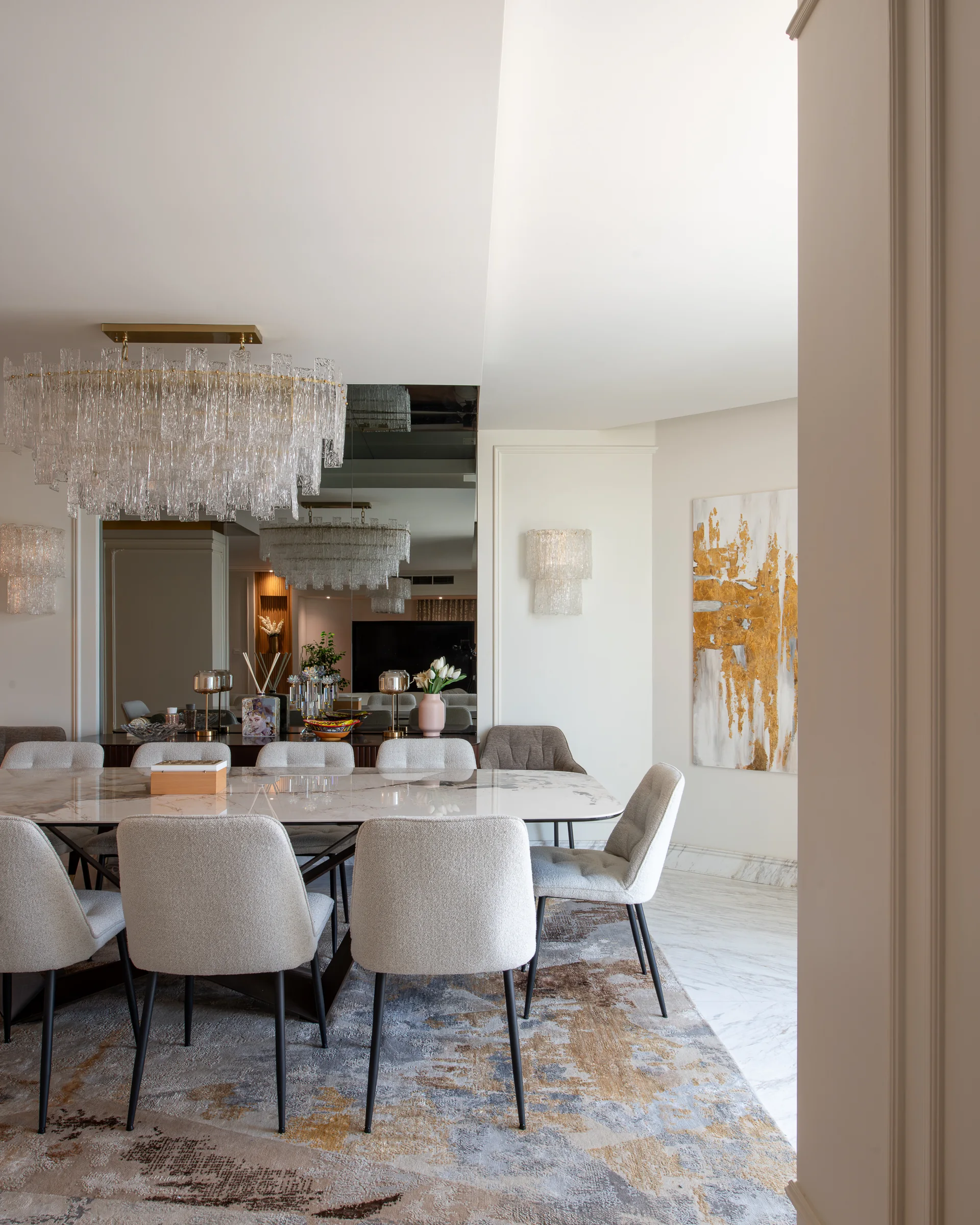 Dining table under its chandelier, mirrored wall behind.