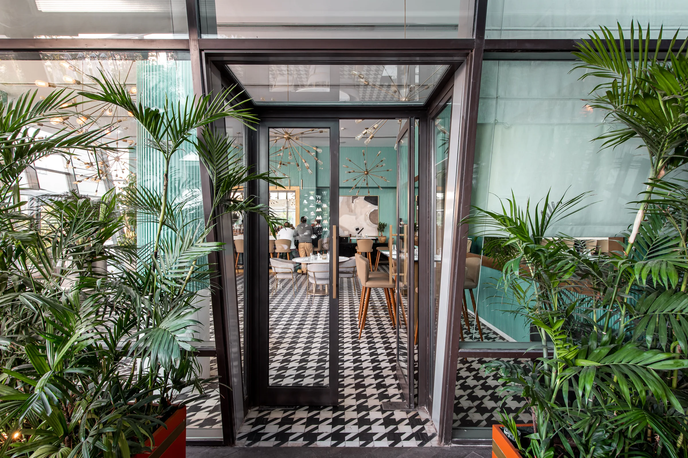 Glazed entrance doors framed by palms over checkerboard tile.