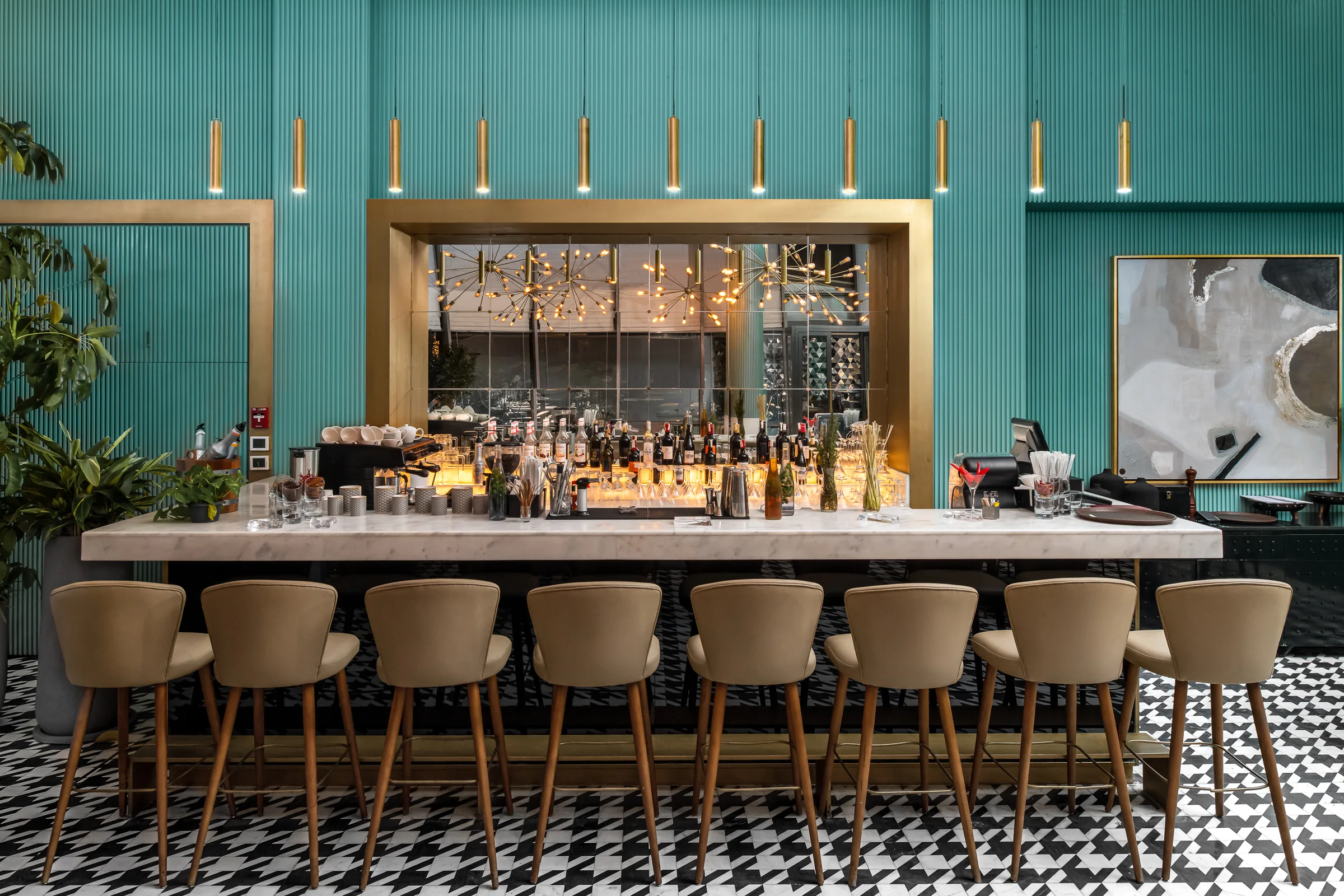 The main bar in marble, brass pendants above a run of stools.